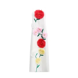 Elegante Detailansicht der bunten 3D-Blumenapplikationen auf einem weißen Maxikleid.
