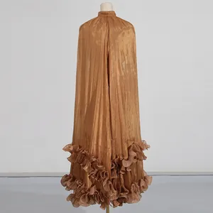 Detalle del dobladillo con volantes y la tela metálica brillante de un vestido maxi de bronce.