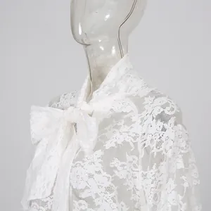 Dettaglio della camicetta in pizzo bianco con un grande fiocco annodato al collo.