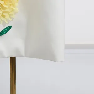 Detailansicht einer großen gelben 3D-Blütenapplikation auf einem weißen Sommerkleid