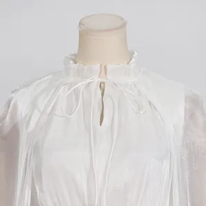 Detalle de un vestido blanco con cuello de volantes y lazos en tejido plisado chic