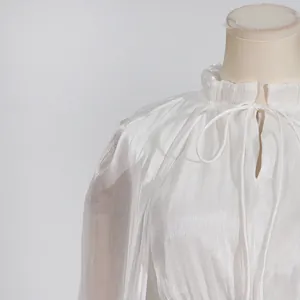 Primer plano de vestido plisado blanco con cuello de volante y detalle de lazo suave