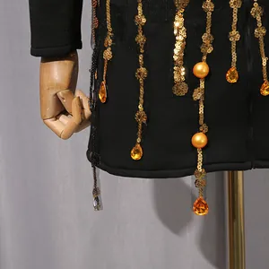 Close-up of black suit dress with gold sequin tassels and amber teardrop gems detail.