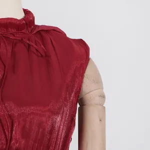 Detalle de vestido rojo vino con cuello alto de volantes y textura plisada brillante
