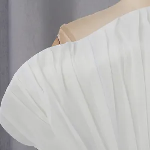 Dettaglio ravvicinato del tessuto bianco a pieghe su un abito monospalla elegante.