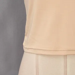 Primo piano dell'orlo della canotta beige che mostra cuciture fini e tessuto liscio.