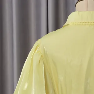 Primo piano del tessuto giallo luccicante e delle maniche a sbuffo di un abito stile retrò