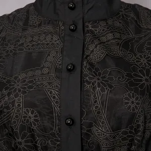 Close-up detail of vintage black dress with intricate embroidery and round buttons.