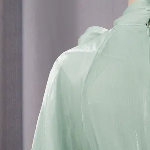 Detalle de primer plano de un vestido de gasa verde menta brillante con elegante cuello alto plisado