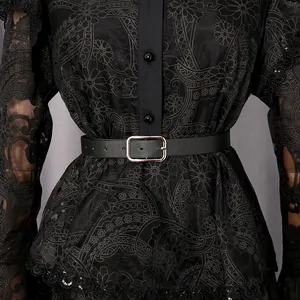 Close-up of intricate black floral lace and leather belt detail on a vintage ruffle dress.