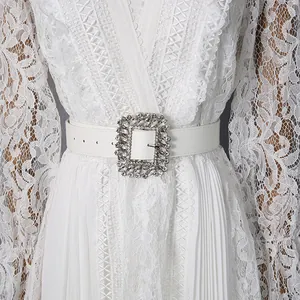 Close-up detail of elegant white lace maxi dress with large rhinestone buckle belt