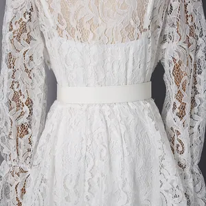 Detail view of a white lace maxi dress with intricate floral embroidery and a matching belt.