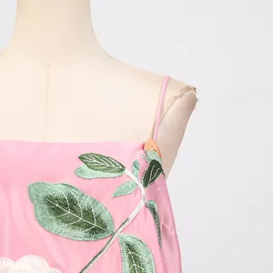 Gedetailleerde close-up van groen bladborduurwerk op een roze satijnen camisole jurk.