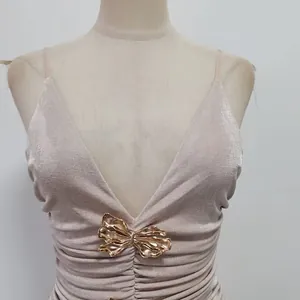 Detailansicht eines champagnerfarbenen Abendkleids mit dekorativer goldener Metallschleife.