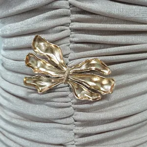 Nahaufnahme der goldenen künstlerischen Metallschließe an einem champagnerfarbenen Faltenkleid