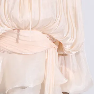 Macro view showing the shimmering pleated texture and tie waist detail of an elegant cream dress