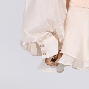 Detailed view of elegant cream dress showing pleated puff sleeve and delicate pearl buttons