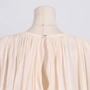 Detailed macro view of the back pleats and button closure on a beige pleated dress.