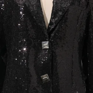 Detalle de una chaqueta de lentejuelas negras con botones cuadrados plateados.