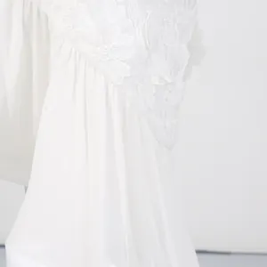 Close-up detail of white holiday dress featuring floral embroidery and pleated fabric texture