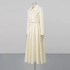 Studio view of an elegant cream two-piece set featuring beaded jacket and pleated skirt