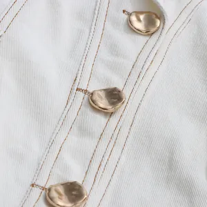 Nahaufnahme goldener unregelmäßiger Kieselknöpfe an einem weißen strukturierten Sommerkleid