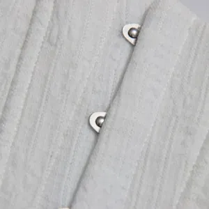 Close-up macro shot of durable silver hook and eye closure on white textured fabric