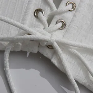 Macro view of white lace-up dress featuring metal eyelets and elegant cross-tie cord detail