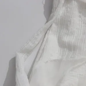 Close-up detail of white halter dress featuring elegant textured fabric and tassels