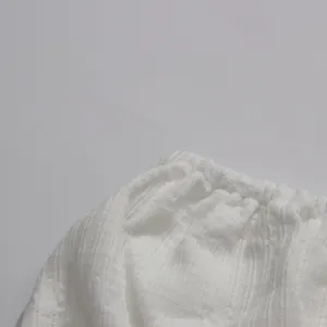 Macro detail of white textured fabric and gathered elastic waistband on the dress.