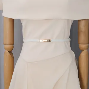 Dettaglio di un elegante abito beige con cintura sottile bianca e fibbia dorata in vita