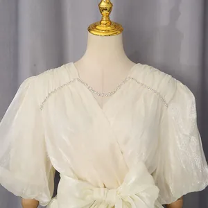 Detailopname van een elegante crème glanzende jurk met V-hals, kristallen rand en pofmouwen.