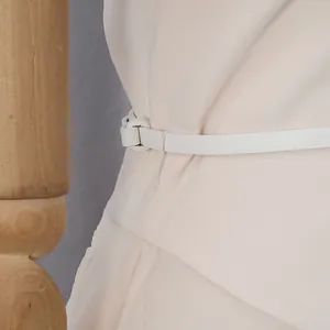 Vista dettagliata della sottile cintura in pelle bianca su un elegante abito beige