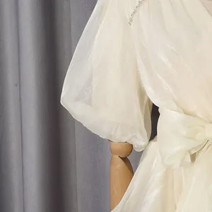 Detail van een crèmejurk met pofmouwen en een elegante strikdecoratie in de taille
