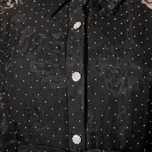 Close-up of crystal flower buttons on black floral textured fabric with silver polka dots.