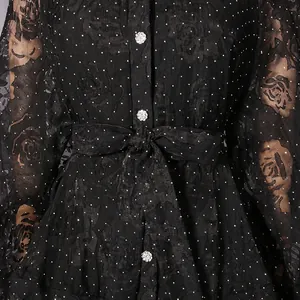 Close-up detail of black floral lace dress featuring decorative crystal buttons and polka dots