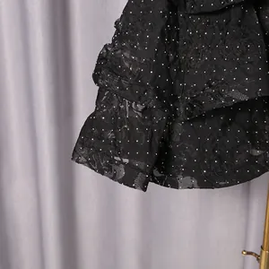 Detail of elegant black dress with floral lace and silver glitter polka dot ruffles.
