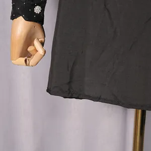 Close-up view of black elegant dress hem and sleeve with rhinestone floral details.