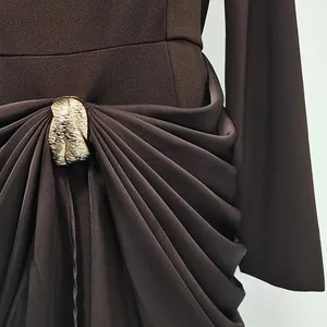 Detailed view of the elegant gold leaf buckle and draped pleats on a brown dress