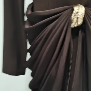 Close-up of brown dress waist featuring elegant draping and a gold metal buckle detail.