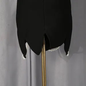 Detailopname van zwart kledingstuk met geschulpte zoom en elegante witte parels aan de rand