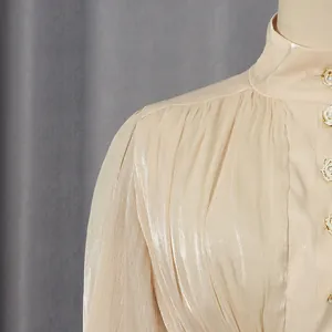 Detail of champagne satin dress with shimmering pleated fabric and floral pearl buttons