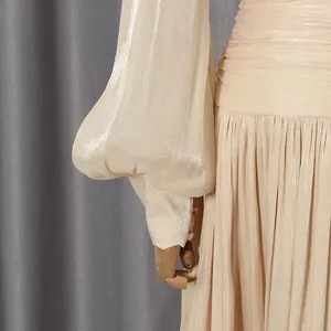 Detail of champagne shimmering pleated dress with elegant lantern sleeves and button cuffs