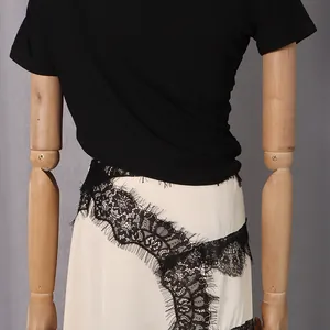 Macro detail shot of the intricate black lace patchwork on a cream-colored elegant dress