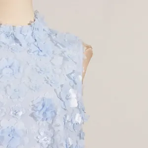 Macro detail of a light blue summer dress featuring 3D fabric flowers and pearls.