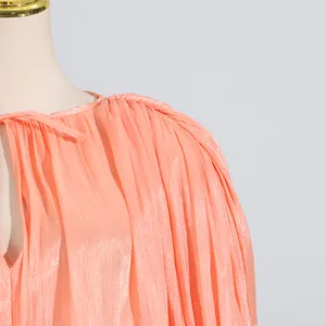 Primo piano di un vestito a pieghe color pesca con elegante fiocco al collo chic.