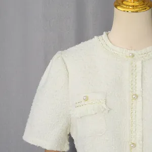 Detail eines weißen Tweed-Kleides mit Perlenknöpfen und Goldfaden
