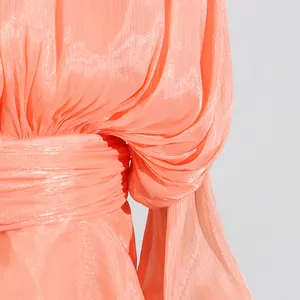 Dettaglio macro di un abito rosa corallo con vita a pieghe e tessuto scintillante