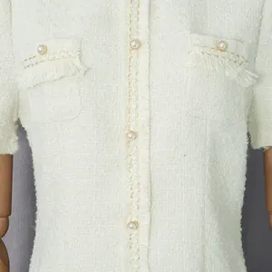 Detailaufnahme eines eleganten Tweedkleides mit Perlenknöpfen und Fransenverzierung.