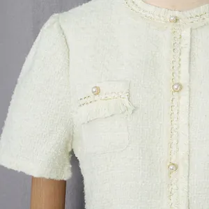 Nahaufnahme eines weißen Tweed-Kleides mit eleganten Perlenknöpfen und feinen Fransen-Details